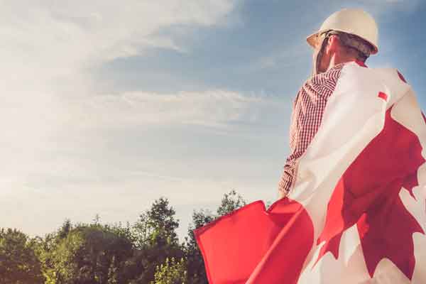 Man in a hard hat with a Canadian flag around him looking off into the distance with a blue sky.